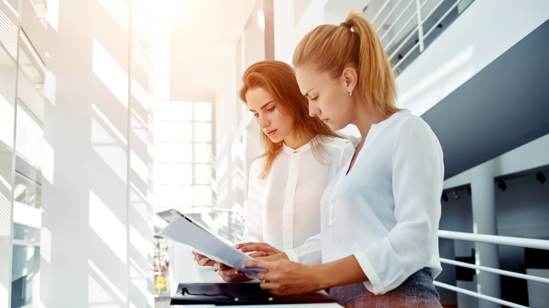 Due giovani donne guardano concentrate un documento, sullo sfondo delle vetrate