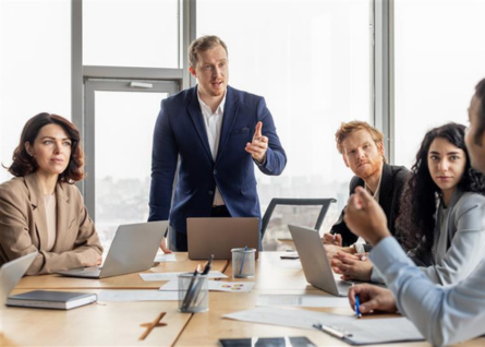 Giovane professionista uomo sta parlando con un gruppo di colleghi riuniti attorno a un tavolo 
