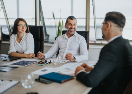 Due professionisti parlano con un consulente, seduti alla scrivania, con fare sorriedente e collaborativo 
