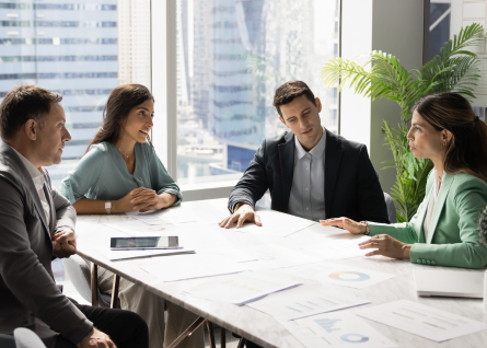 Un gruppo di professionisti, uomini e donne, parlano con focus riunti attorno a una scrivania 